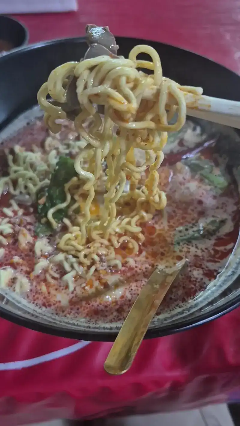 Noodles lifted from a bowl of red broth
