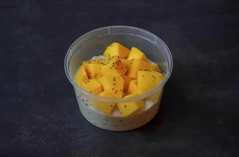 Overnight oats with chia, topped with cubed mango, in a round tub
