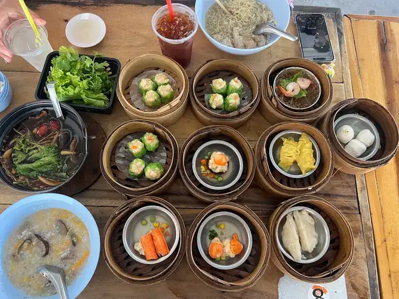 A table of dim sum baskets with a bowl of bak kut teh and greens, rice porridge and a bowl of noodle soup