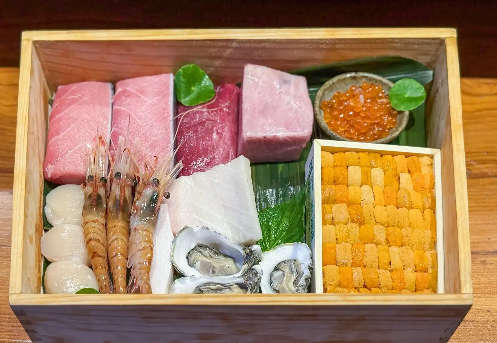 Tuna, sea urchin, salmon roe, scallops, prawns and oysters laid out in an open wooden box