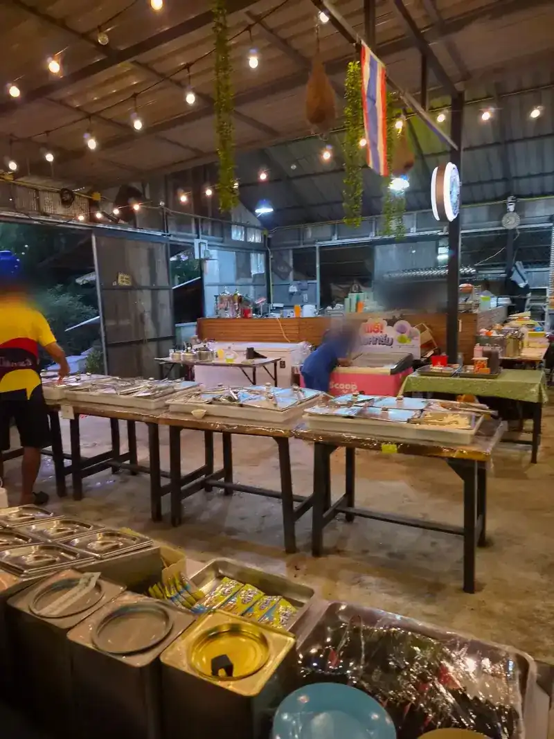 The buffet hall at dusk: long tables of covered steel trays under string lights and a tin roof