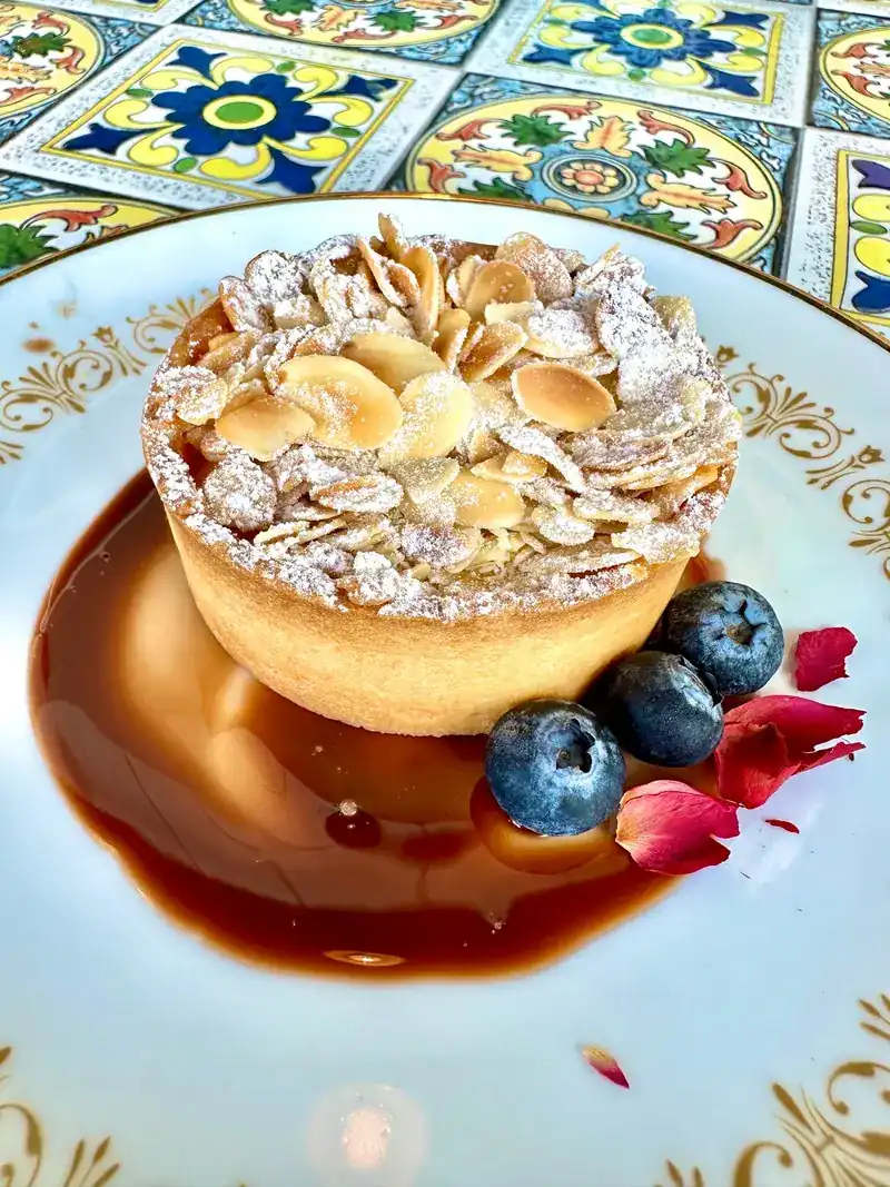Tart topped with flaked almonds, served with blueberries on a tiled table