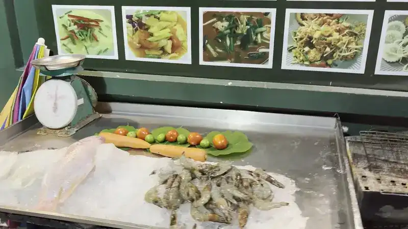 Fresh fish and prawns laid out on ice, with photos of dishes on the green wall above