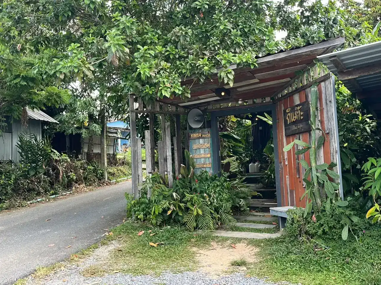 The wooden gate of Kinta Mini Cafe under the trees, beside a small lane