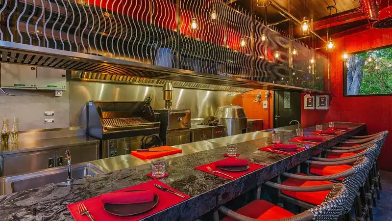 The long stone counter with red place settings facing the open grill kitchen