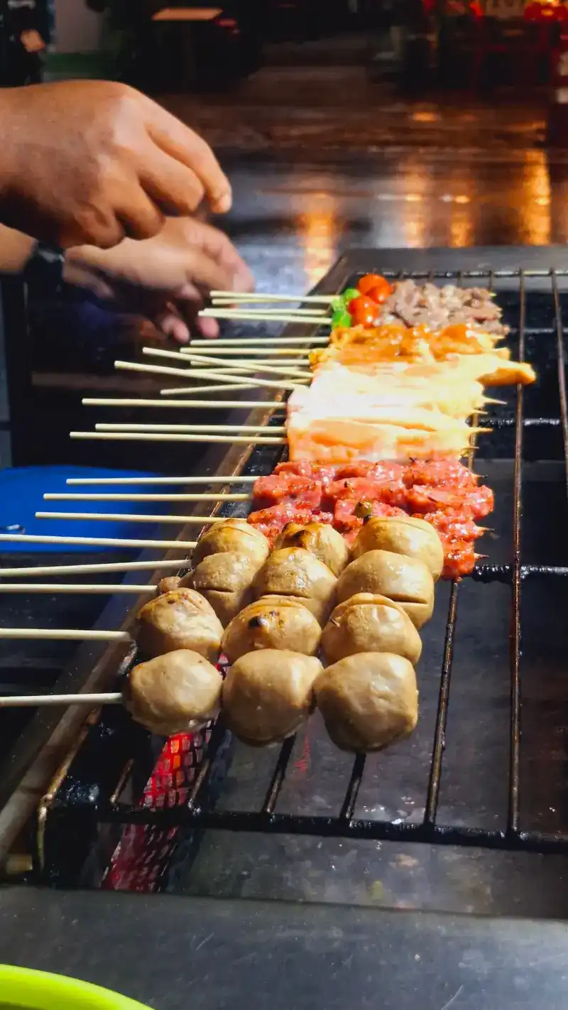 Hands laying skewers of meatballs, chicken and beef on the grill