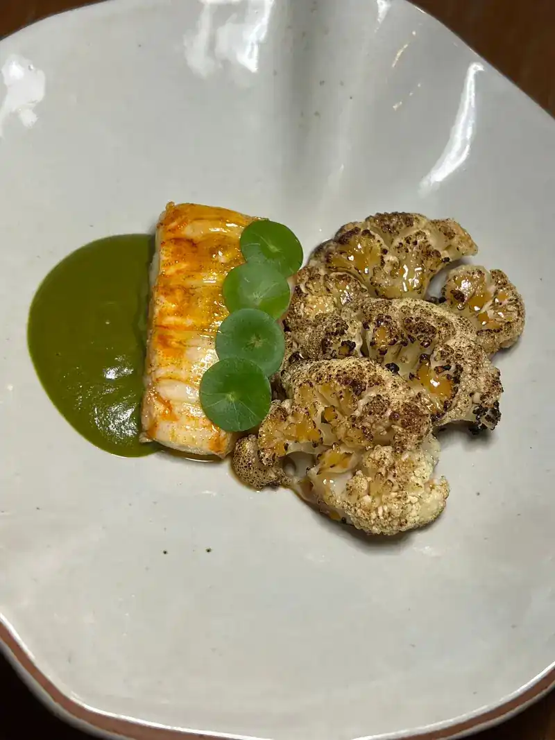 Seared fish with a green sauce and roasted cauliflower on a grey plate