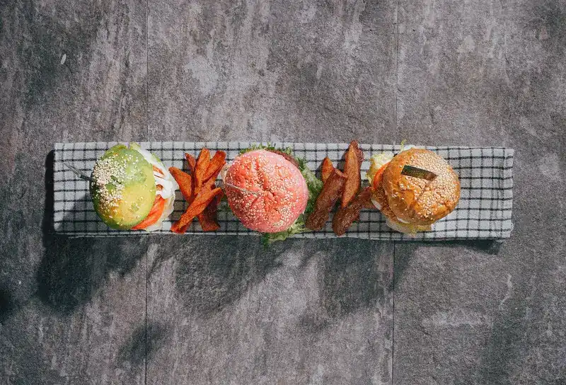 Three small burgers with different coloured buns and potato wedges on a checked cloth