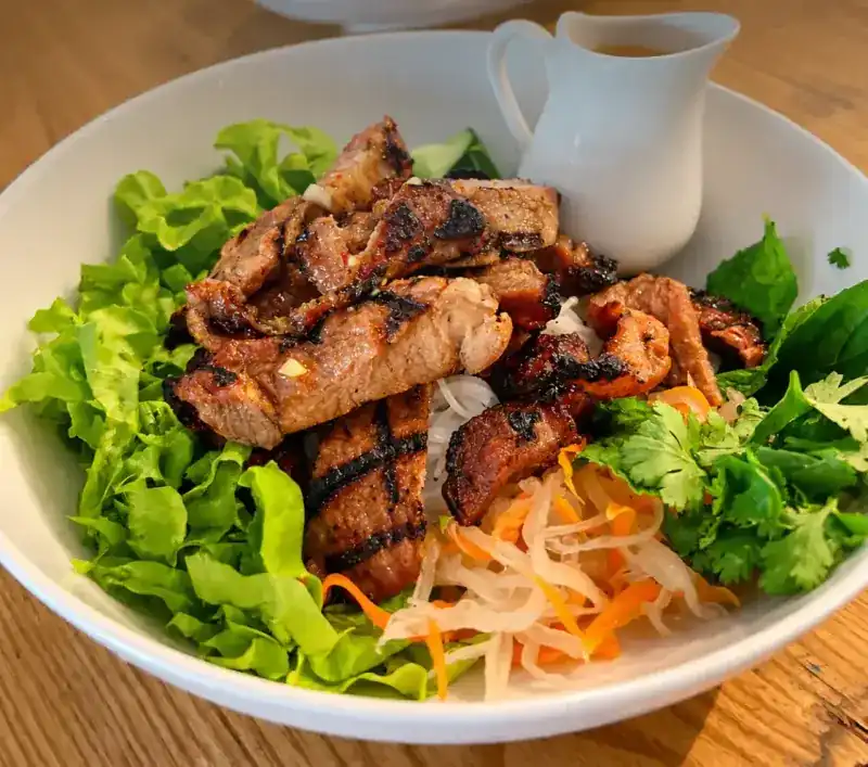 BBQ Pork Bowl: grilled pork over lettuce, herbs and pickled vegetables, with sauce in a small jug