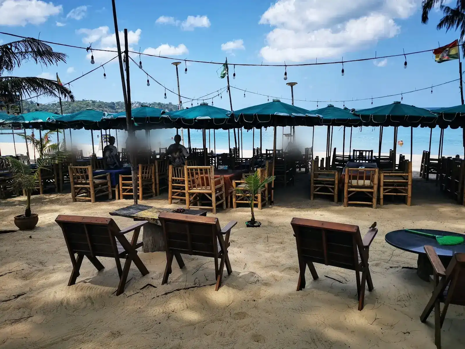 Bamboo chairs and teal umbrellas on the sand at Big Bump, with the sea of Bang Tao behind