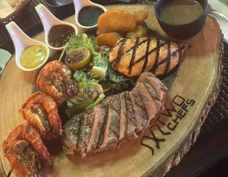 Grilled prawns, salmon and sliced steak with salad on a wooden board