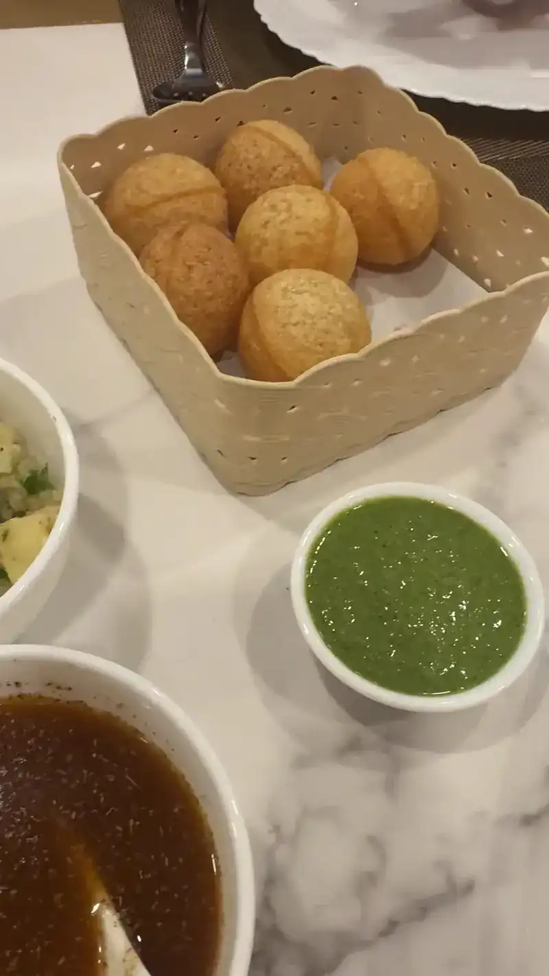 Pani puri shells in a basket with green chutney and spiced water