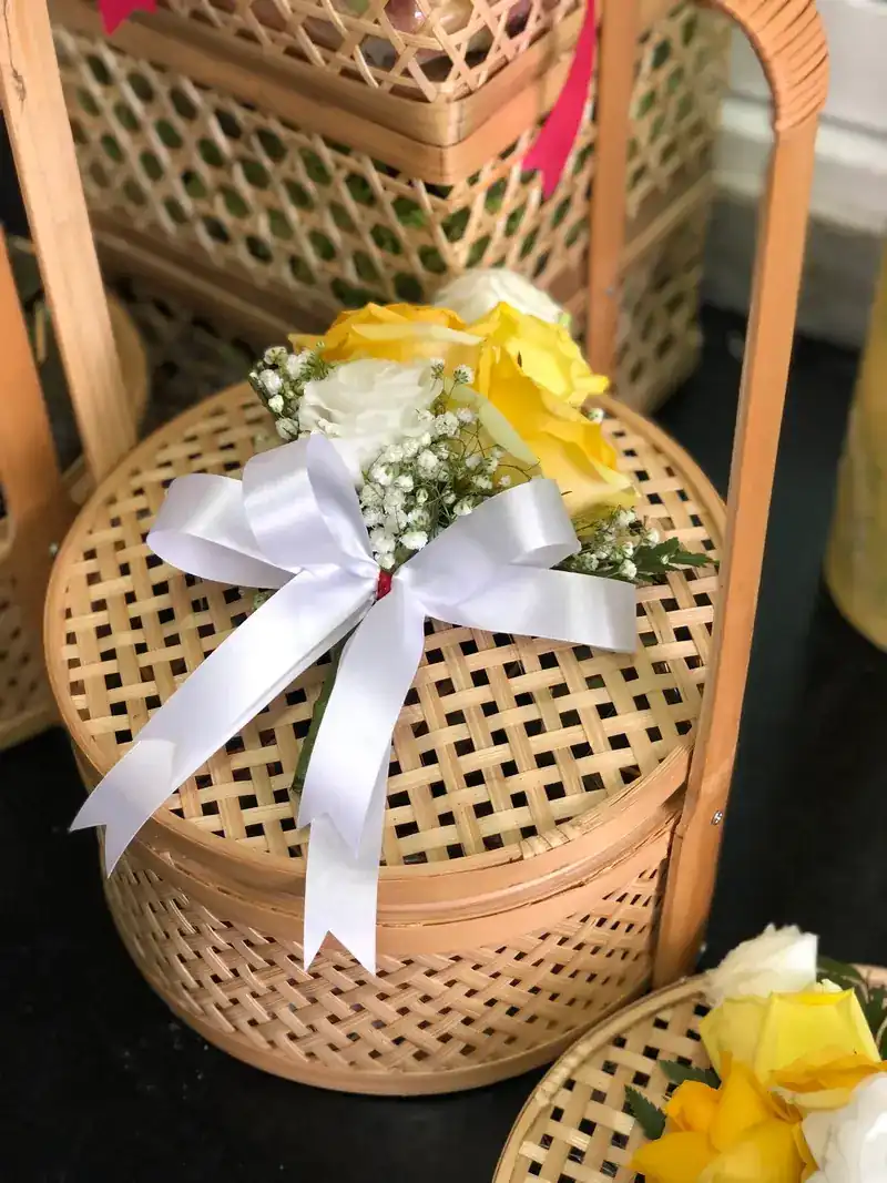 A woven bamboo gift basket tied with a white ribbon and yellow roses