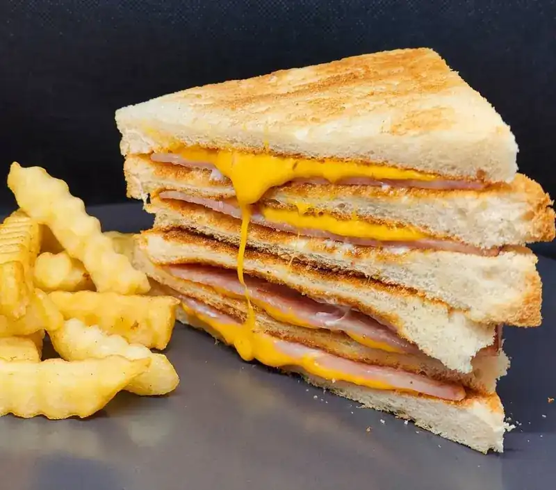 Toasted ham and cheese sandwich cut in half, with crinkle-cut fries