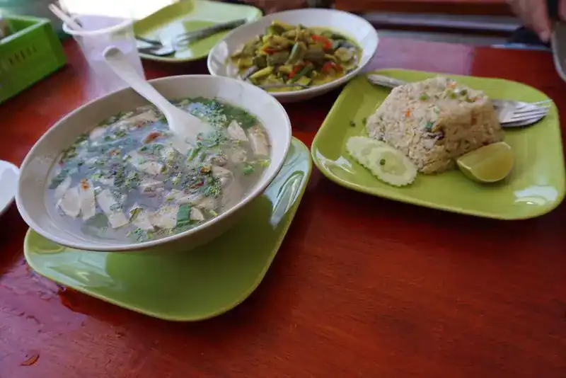 A bowl of clear soup with fried rice and a vegetable stir-fry on a red table