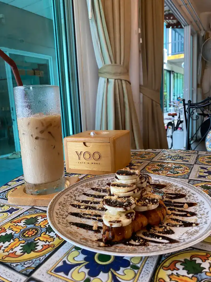 Iced latte and a pastry topped with banana and chocolate, beside a wooden YOO box