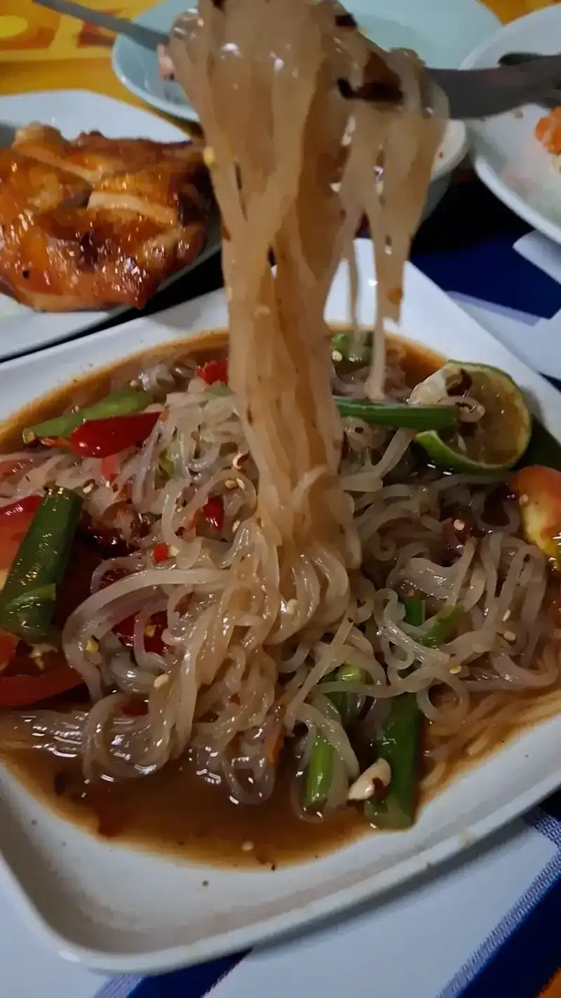 Noodles lifted with a fork from a plate of spicy pounded salad with long beans and chilli