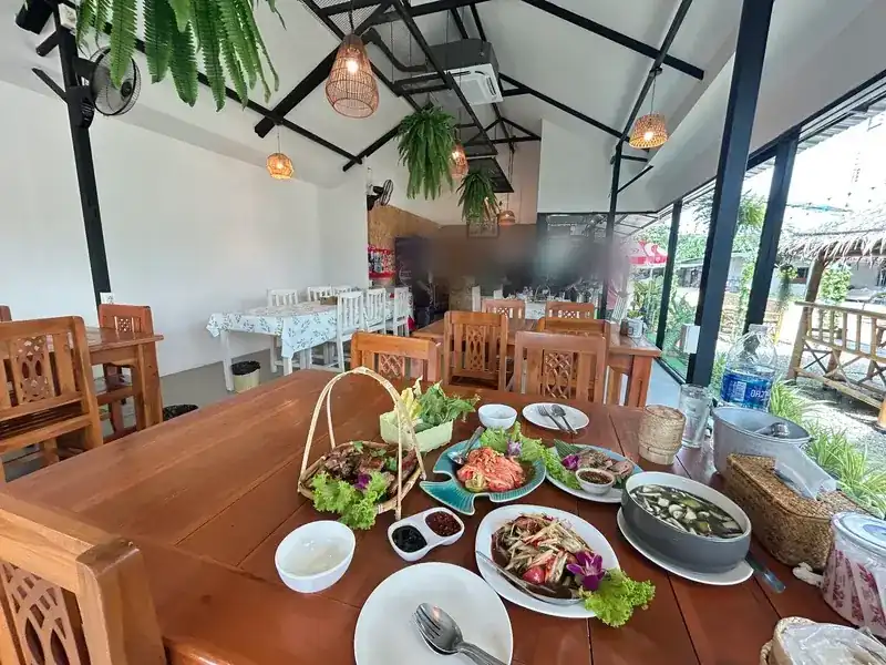 The dining hall: wooden tables, hanging ferns and rattan lamps, with an Isan meal laid out in front
