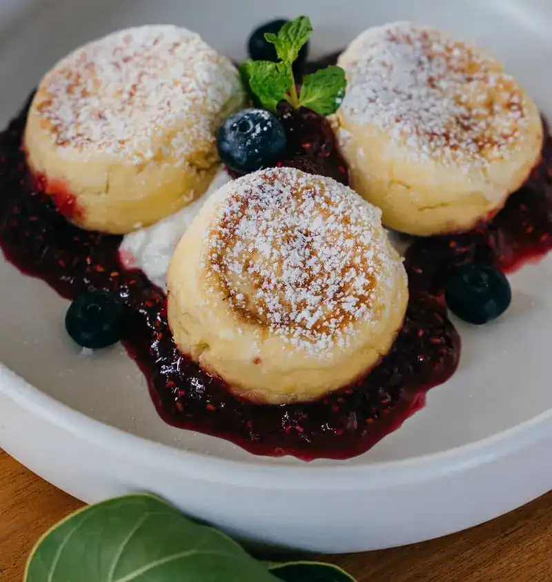 Three syrniki dusted with sugar on raspberry jam with blueberries