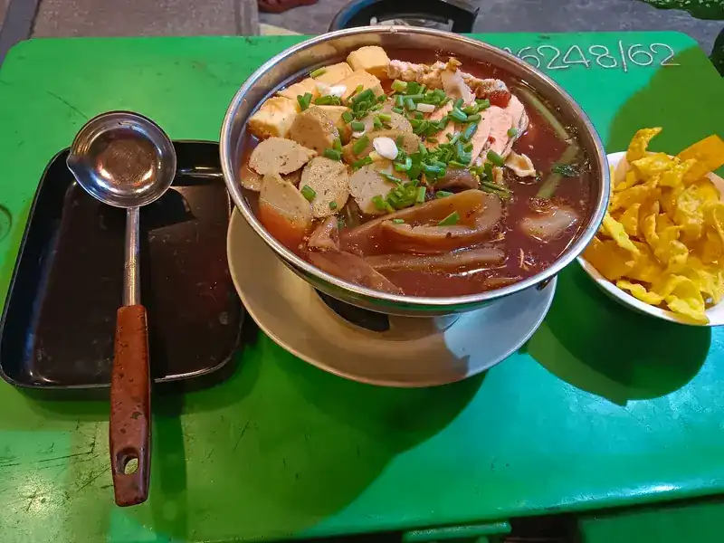 A hot pot on its burner with meatballs, tofu and spring onion, crisp wonton strips on the side