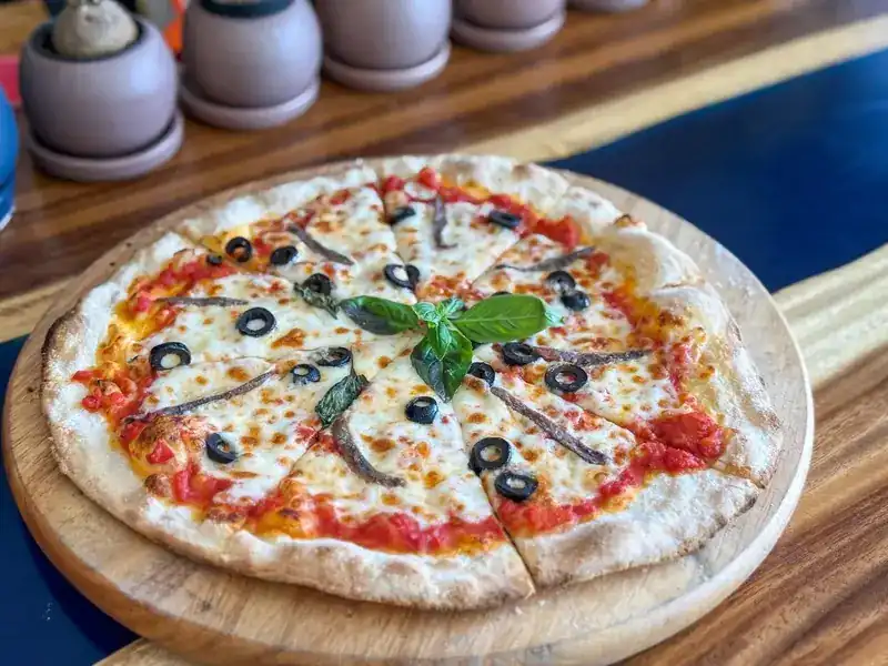 A thin-crust pizza with tomato, mozzarella, anchovies, black olives and basil on a wooden board