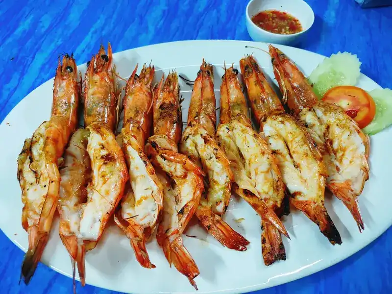 Grilled prawns, split open, on a white plate with dipping sauce