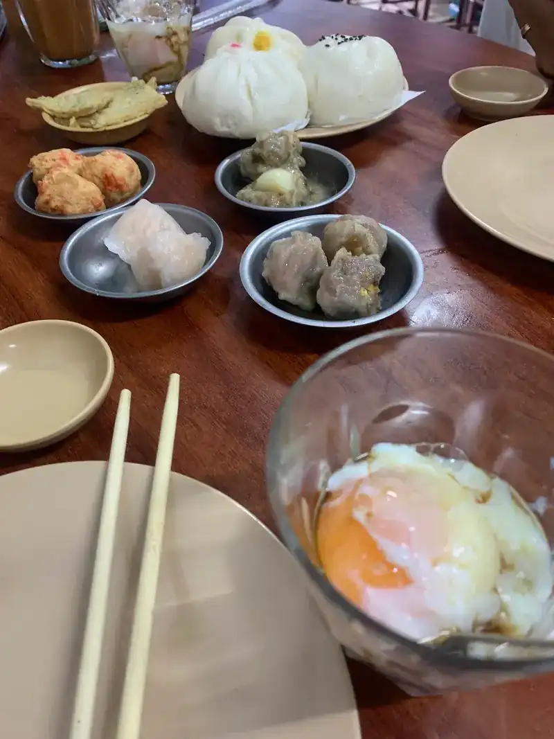 Buns, dim sum in saucers and a soft-boiled egg in a glass bowl