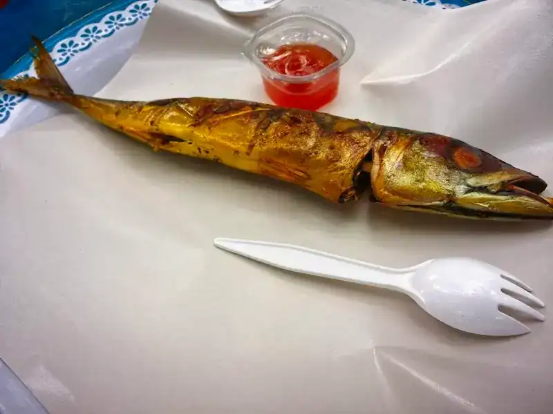 A whole grilled fish on paper with a cup of red dipping sauce