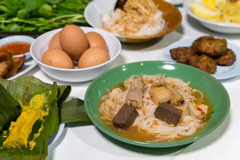 Khanom jeen with chicken curry, boiled eggs, fish cakes and fresh greens