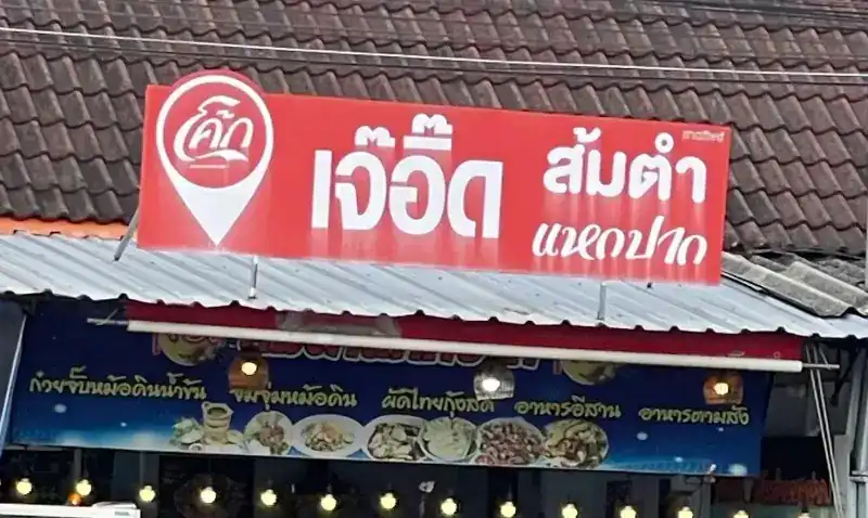 The red sign reading เจ๊อี๊ด ส้มตำแหกปาก above the blue banner and the shop's lights