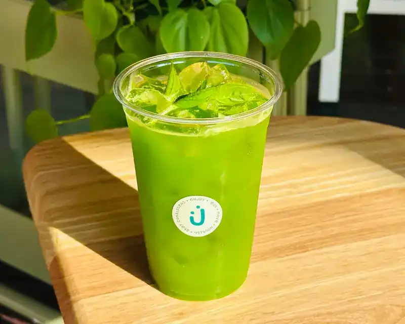 An iced green drink in an Enjoy cup on a wooden table