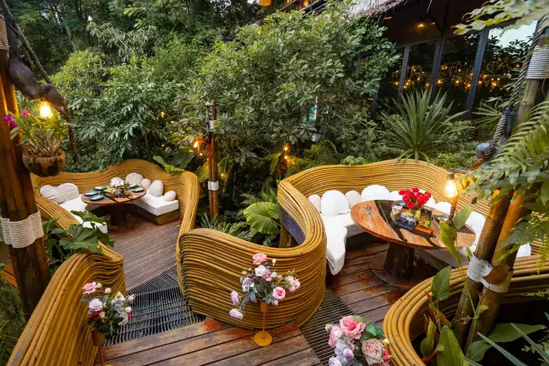 Curved woven rattan seats with white cushions, raised among the leaves