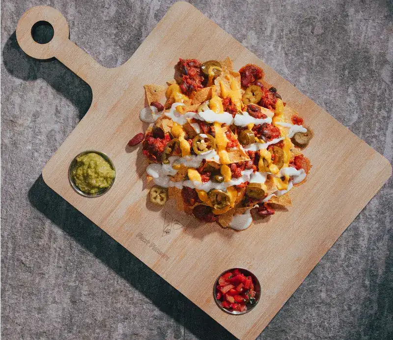 Loaded nachos on a wooden board with guacamole and salsa