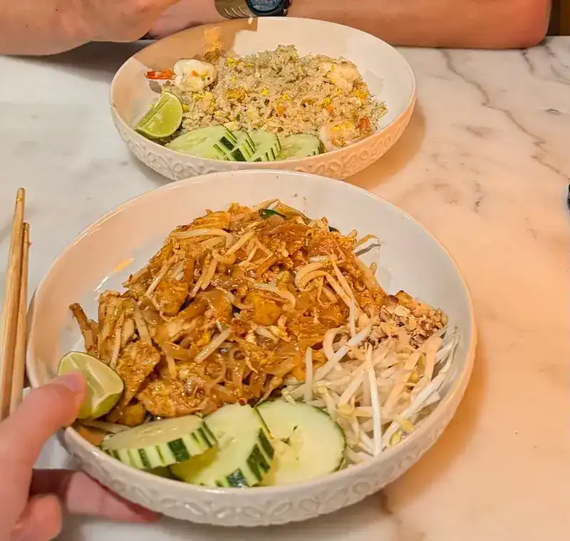 Pad thai with bean sprouts, lime and cucumber, and a bowl of fried rice behind it