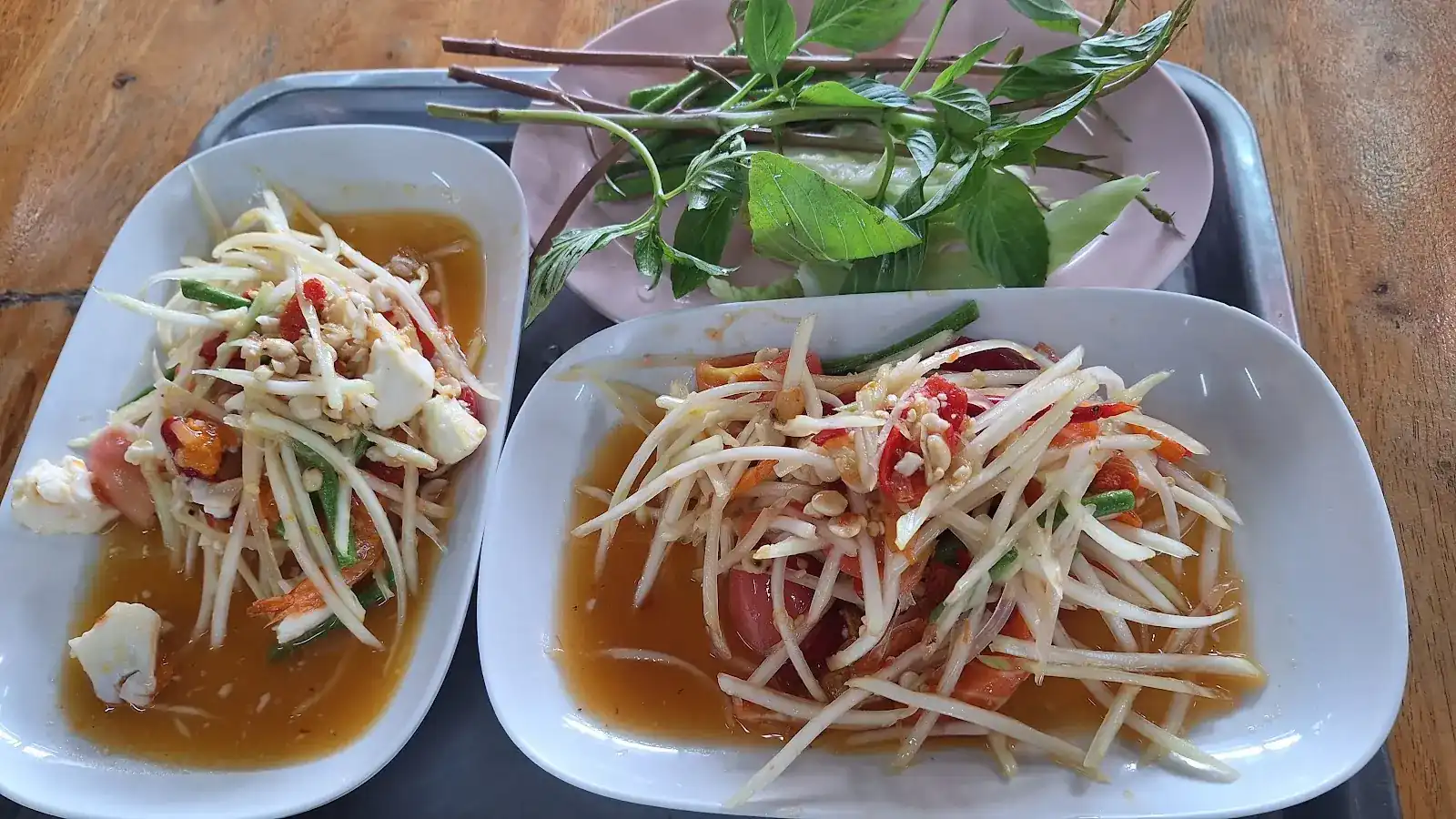 Two plates of som tam on a tray, with fresh herbs