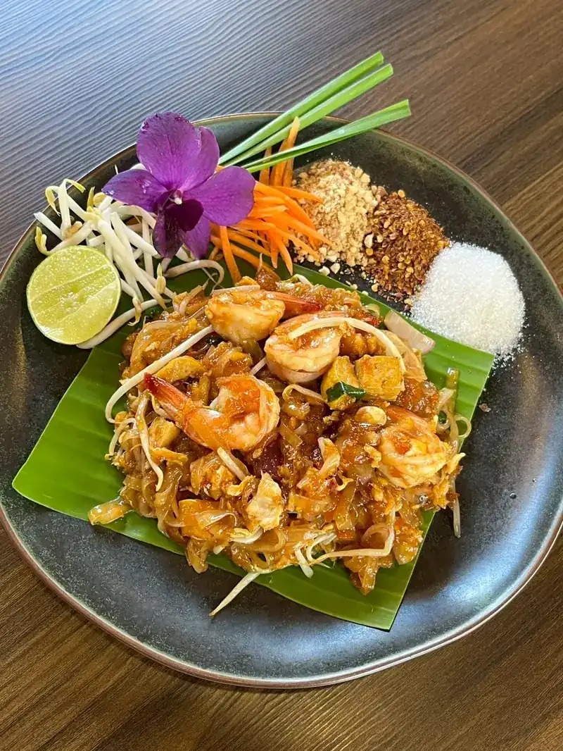 Shrimp pad thai on a banana leaf with lime, peanuts, bean sprouts and an orchid