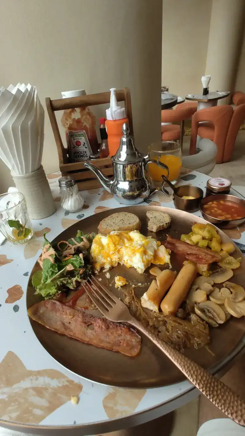 A full breakfast plate with scrambled eggs, sausages, mushrooms, potatoes and salad, a silver teapot behind