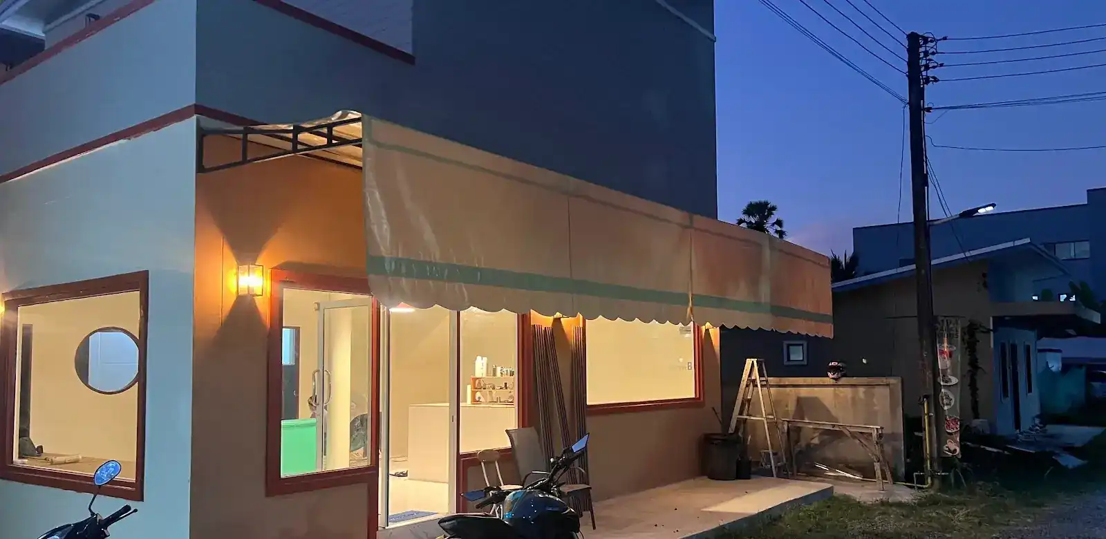 FA&NA at dusk: a corner shop with a beige canvas awning, lit wall lamps and big windows
