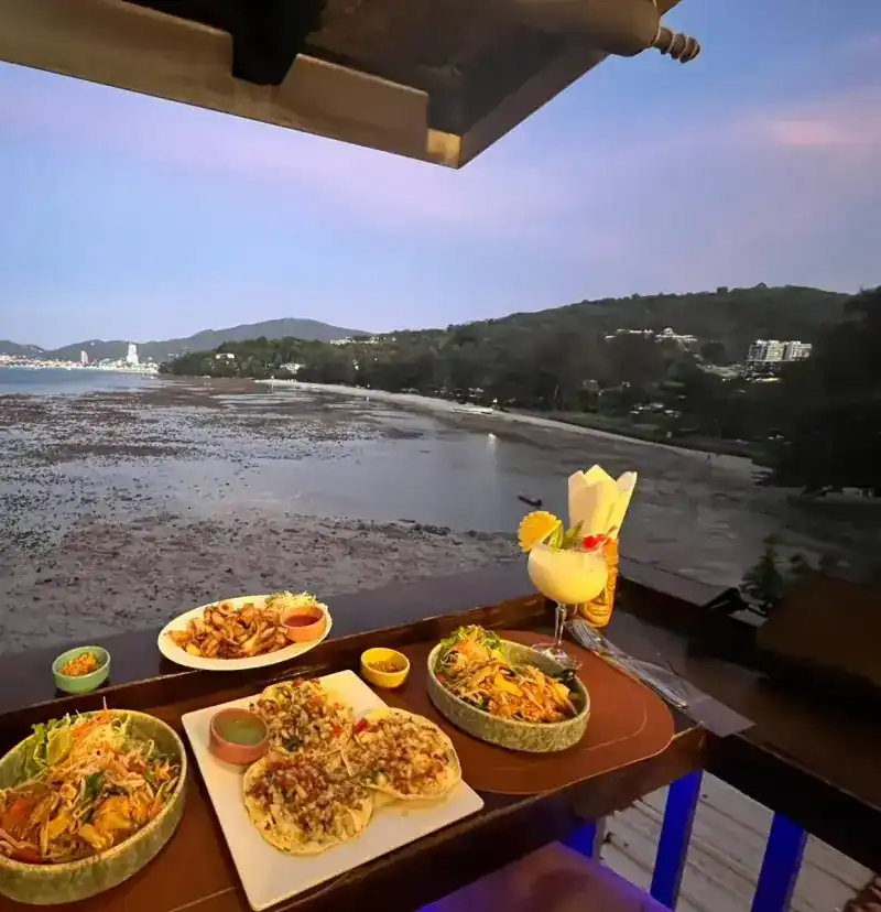 The bay at dusk seen from the railing, with Thai dishes and a drink on the ledge.