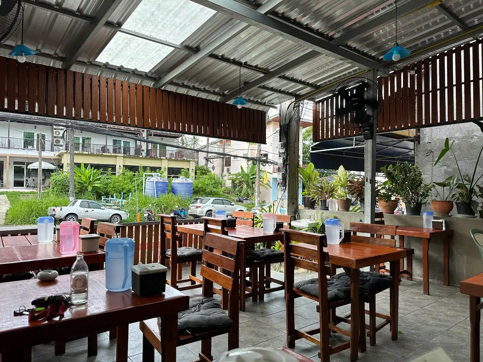 The open-sided dining room at Nok: wooden tables and chairs, fans and potted plants