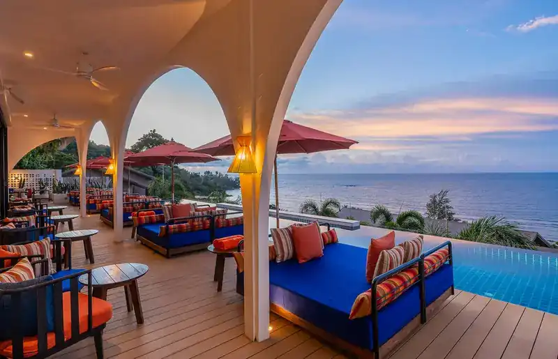 Blue daybeds with striped cushions beside the pool, looking out to sea at dusk