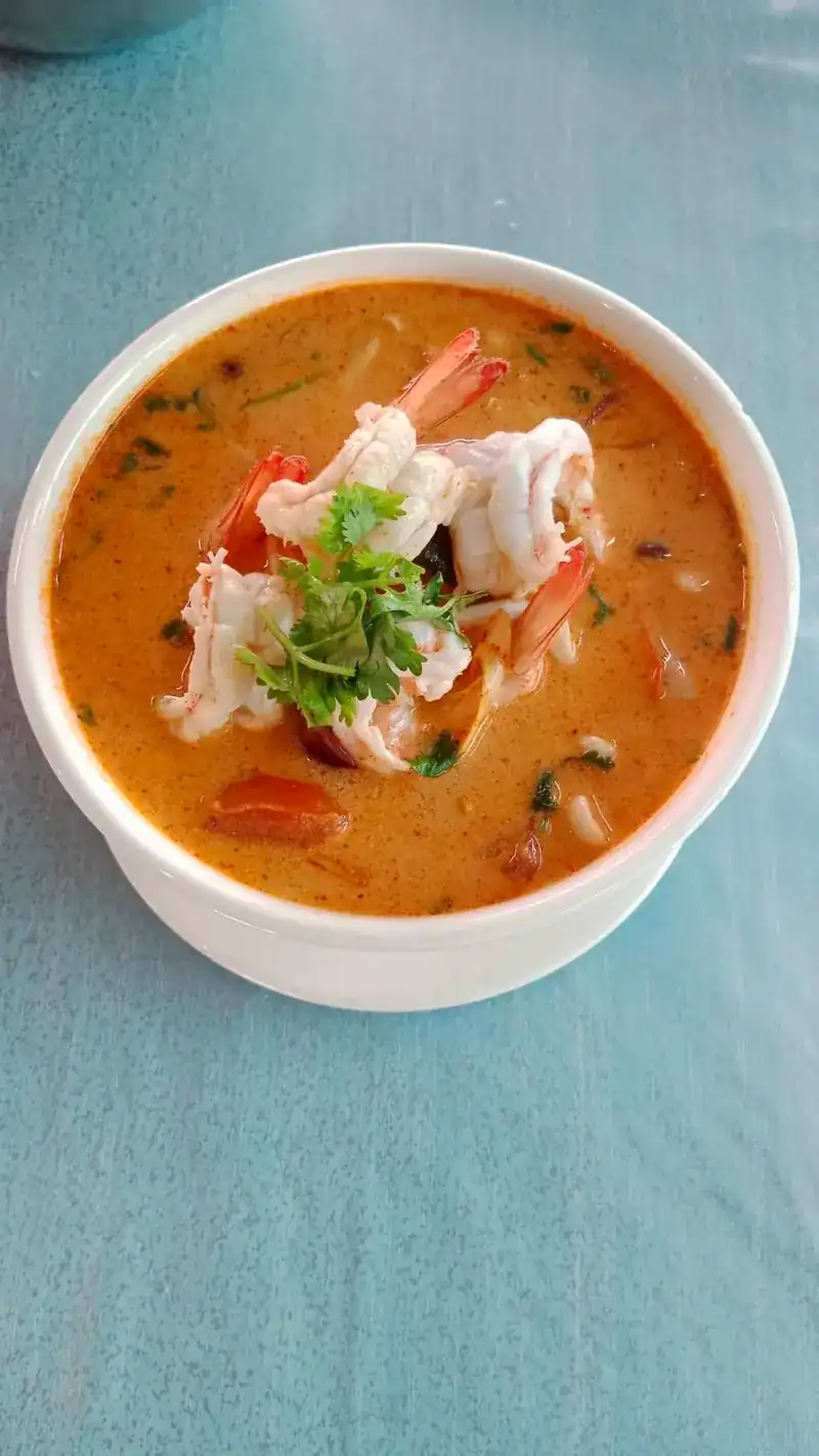 Prawns in a creamy orange soup with coriander, in a white bowl