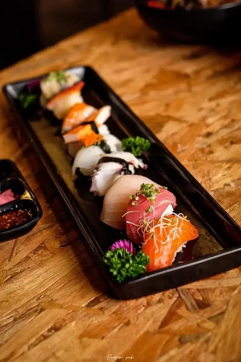 A row of nigiri on a long black plate on a chipboard table