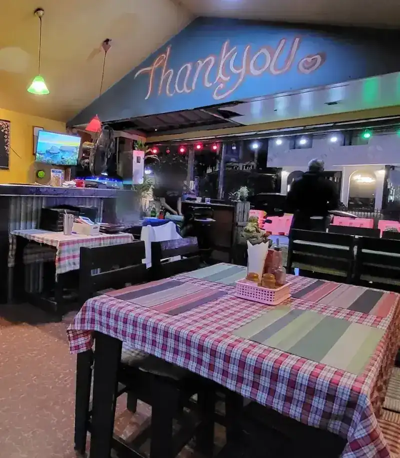Thank you painted by hand on the blue beam above the open front, over a table with a checked cloth