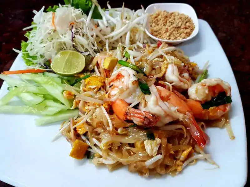 Pad Thai with prawns, lime, crushed peanuts and fresh vegetables on a white plate