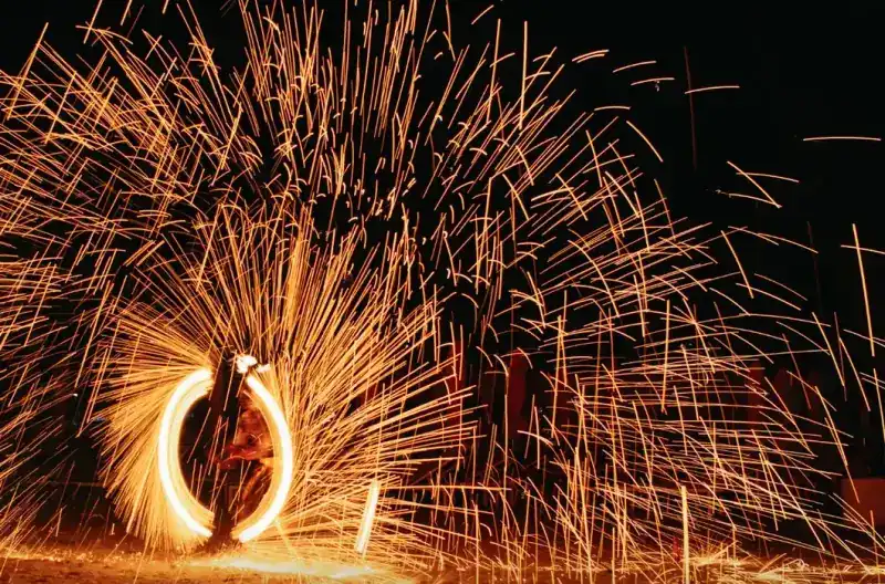 A fire performer spinning a ring of sparks on the beach at night