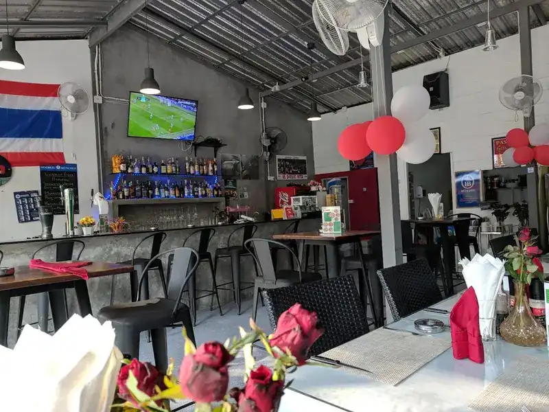 The bar inside, with stools, pendant lamps, ceiling fans and roses on the tables