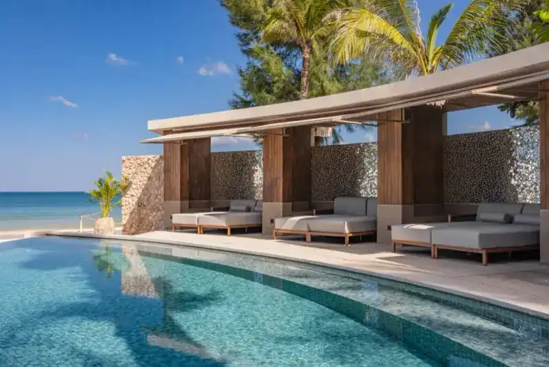Covered cabanas along a curved pool beside the beach