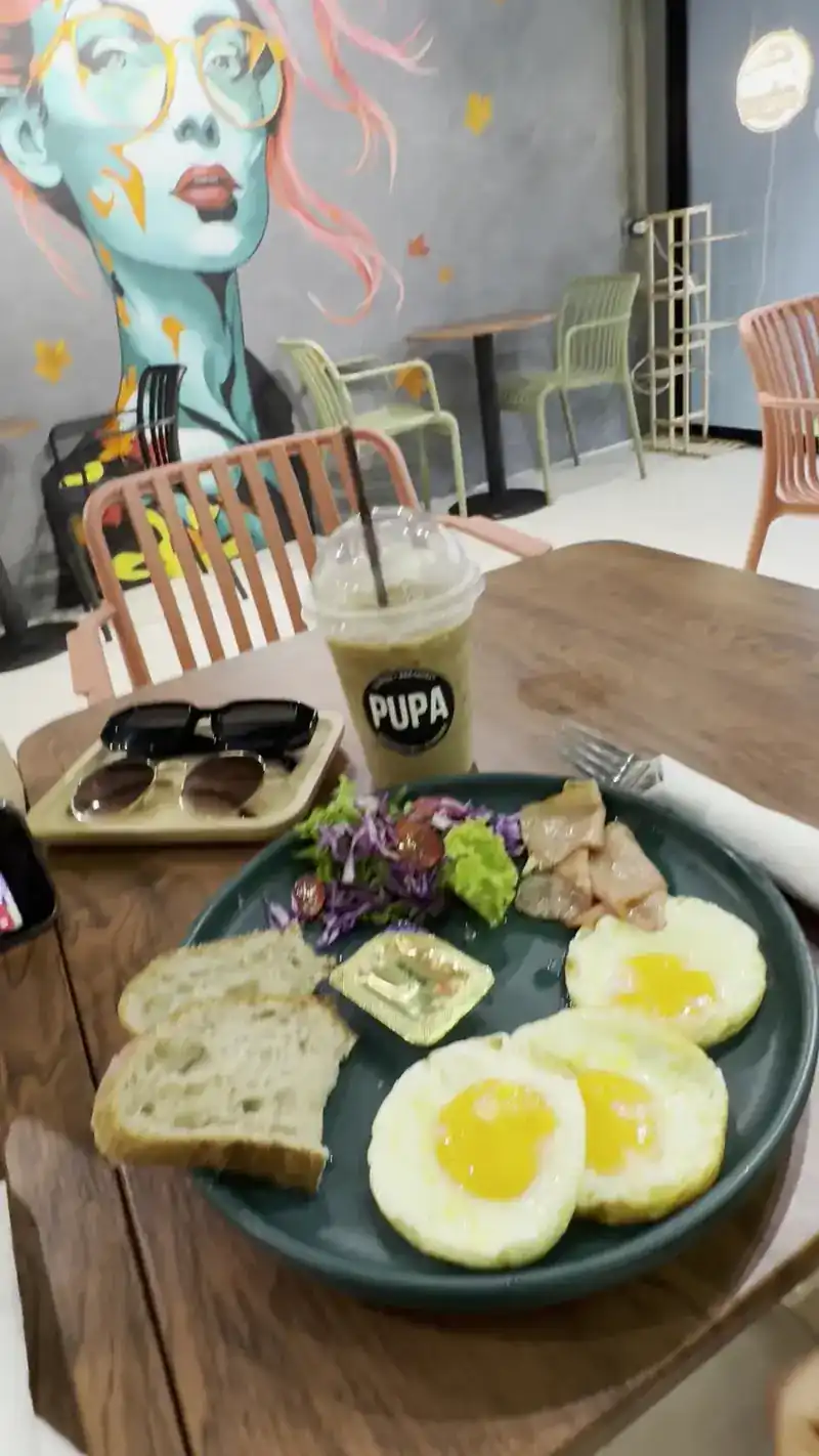Fried eggs, toast and salad with an iced drink in a Pupa cup, the mural behind