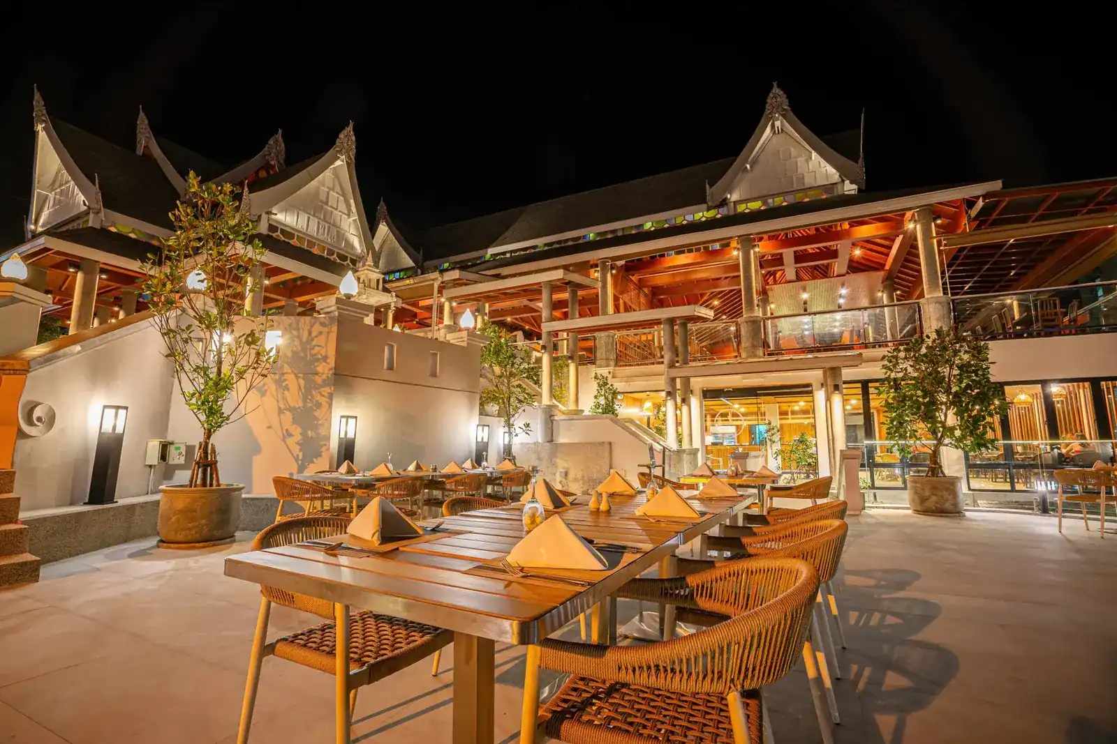 The outdoor tables at night, set for dinner under the lit Thai roofs of Orchidacea Resort